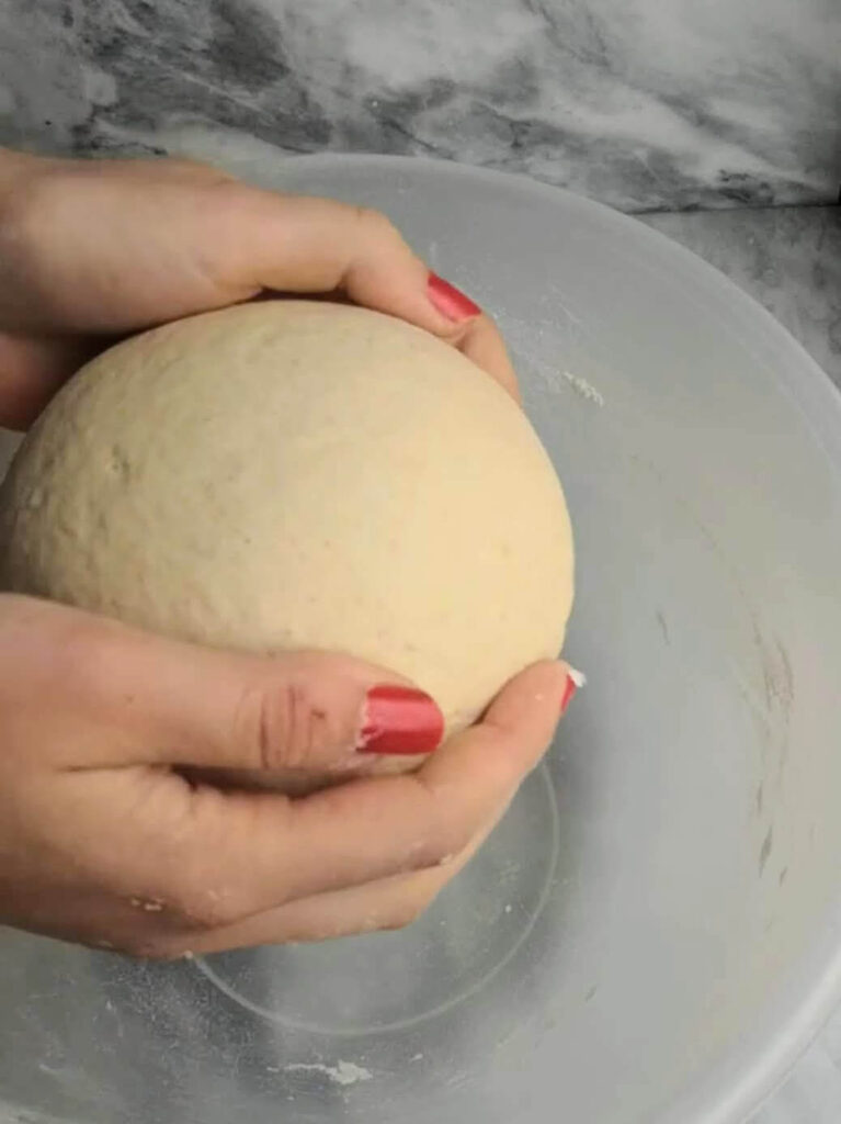 Hands placing the ball of easy soft flatbread dough into a large clear mixing bowl.