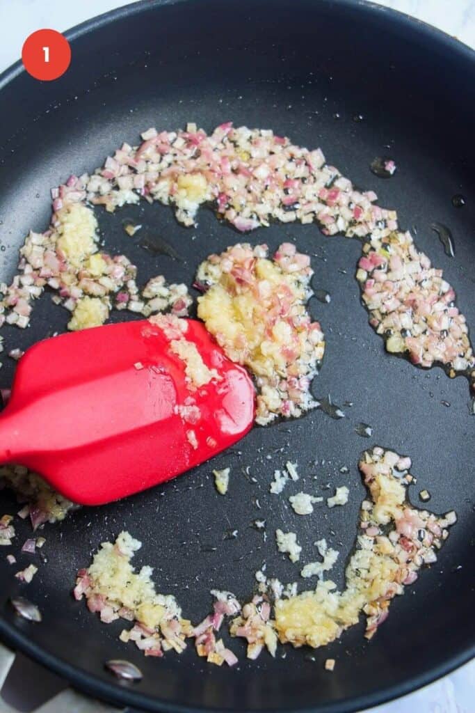 Spatula stirring onion and garlic in a skillet.