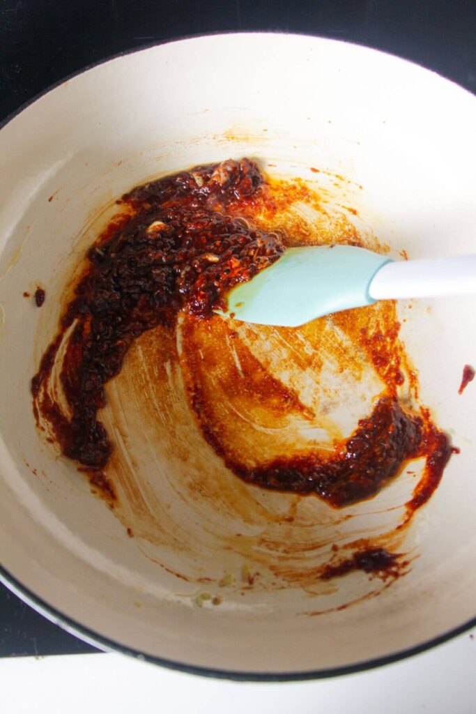 White and blue spatula stirring gochujang paste in a large white skillet.