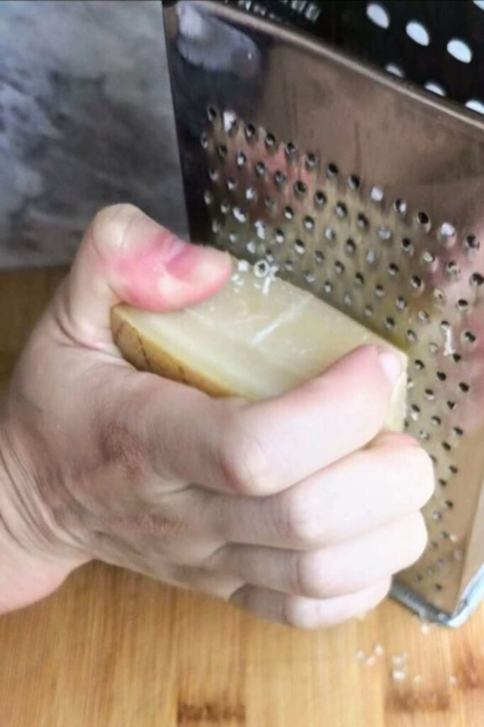 Hand holding a wedge of parmesan cheese against a silver grater.