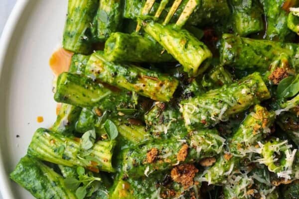 Super green rigatoni with chilli oil drizzled on top on a white plate with a gold fork.