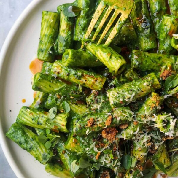 Super green rigatoni with chilli oil drizzled on top on a white plate with a gold fork.