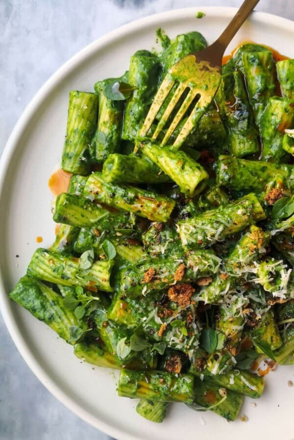 Super green rigatoni with chilli oil drizzled on top on a white plate with a gold fork.