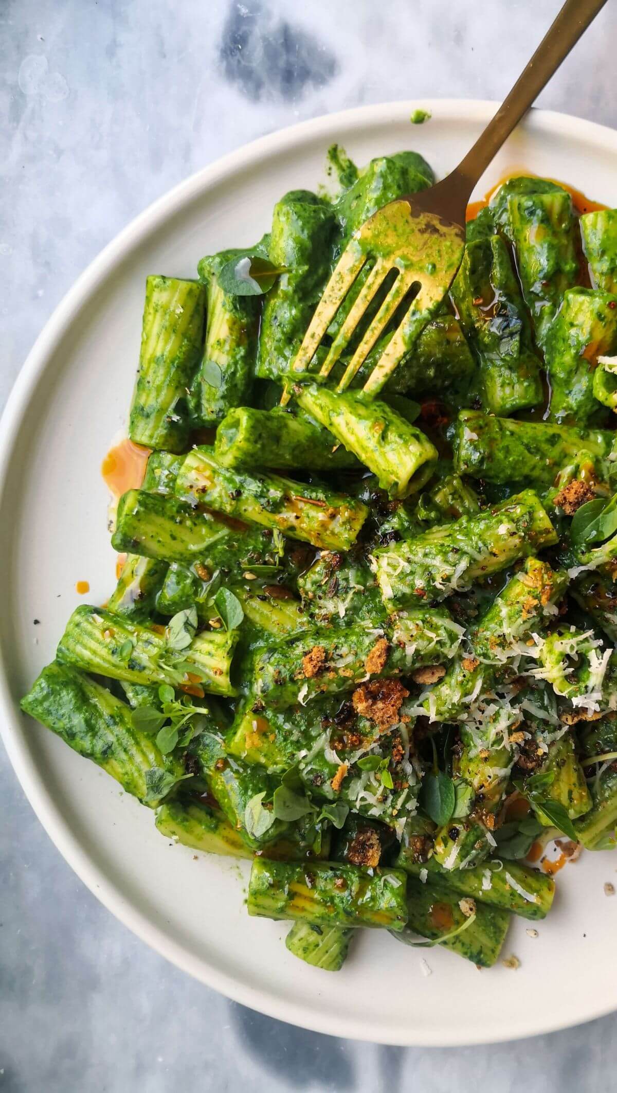 Super green rigatoni with chilli oil drizzled on top on a white plate with a gold fork.