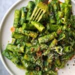 Green pasta sauce with rigatoni on a white plate, with gold fork piercing a piece of pasta.