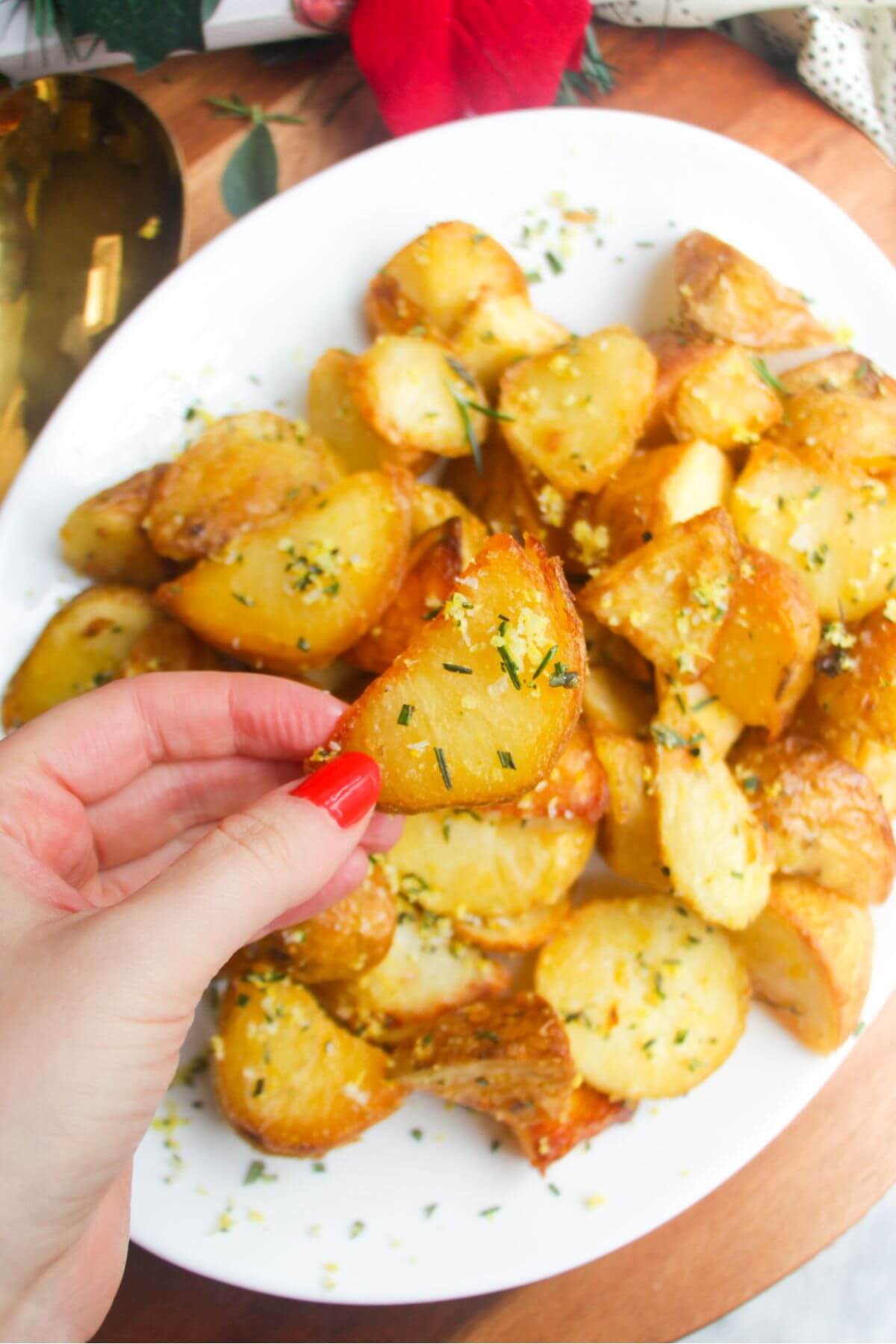 Close up of hand holding up a crispy potato with plate of potatoes in the background.