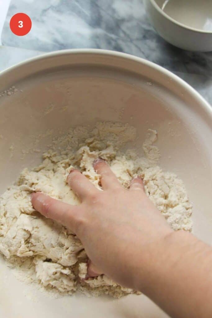 Hand kneading pizza dough in mixing bowl.