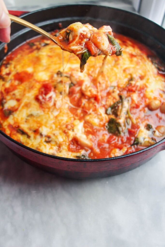 A spoon scooping up cheesy tomato white bean bake with long mozzarella cheese pull.