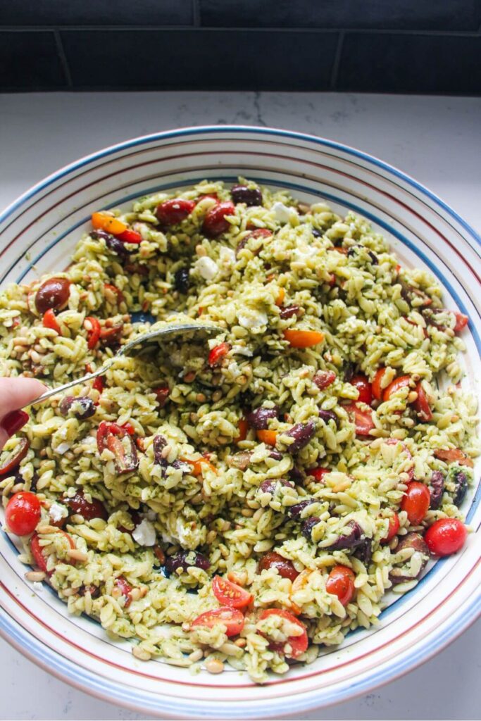 Orzo pesto salad being mixed in a large serving plate.