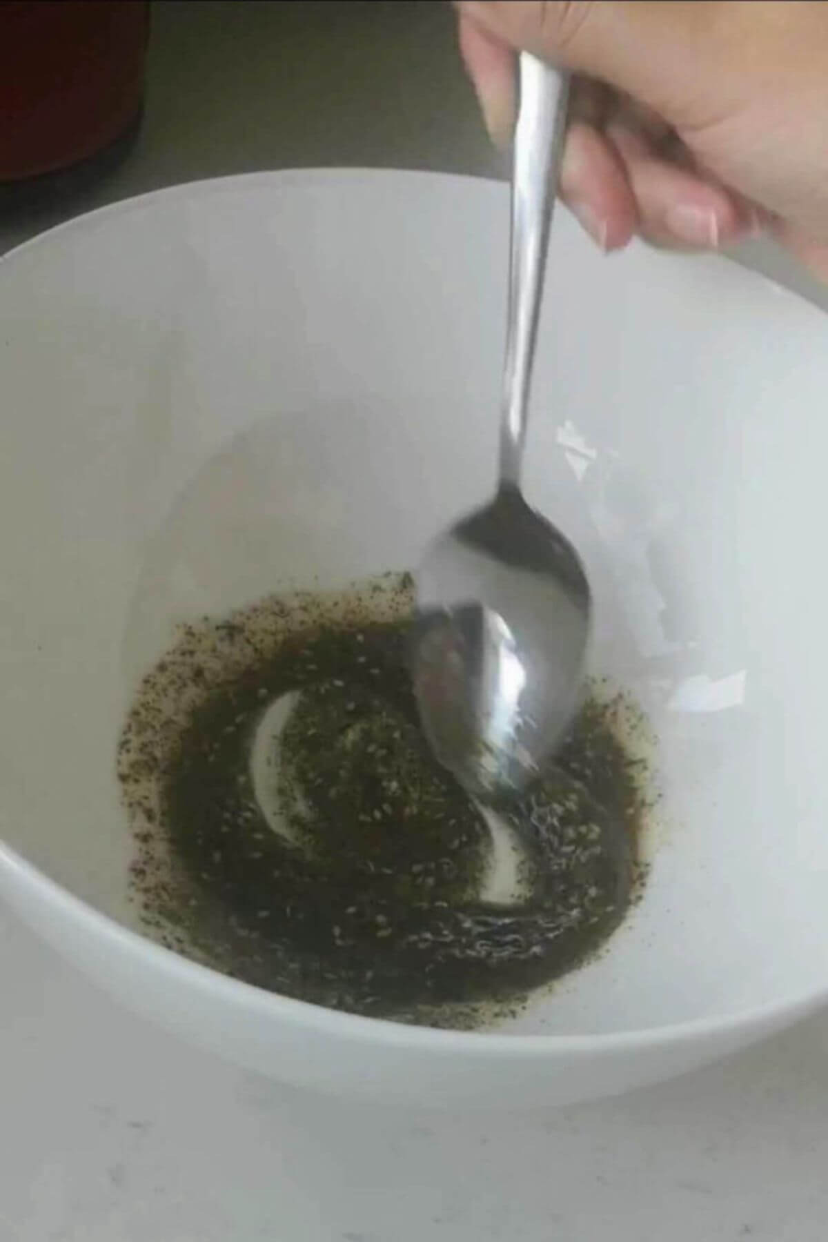 Silver spoon mixing za'atar and oil in a large white bowl.