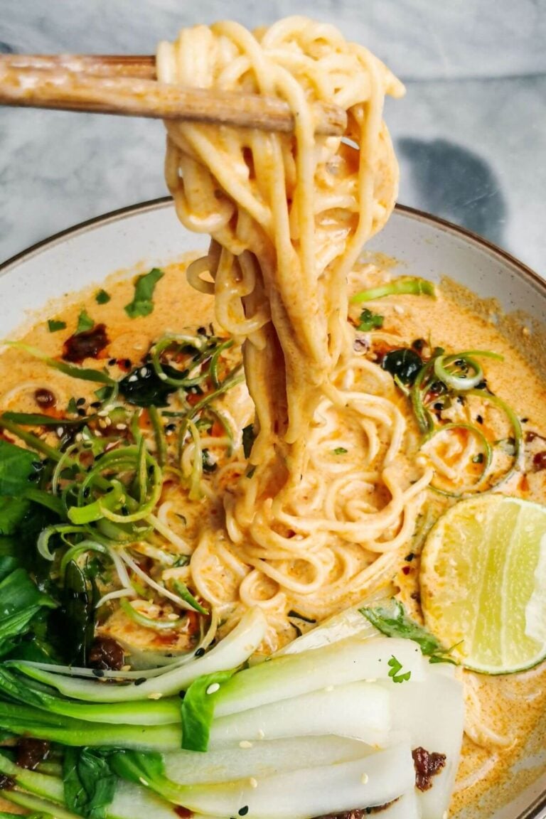 Chopsticks pulling up saucy coconut noodles in a white bowl.