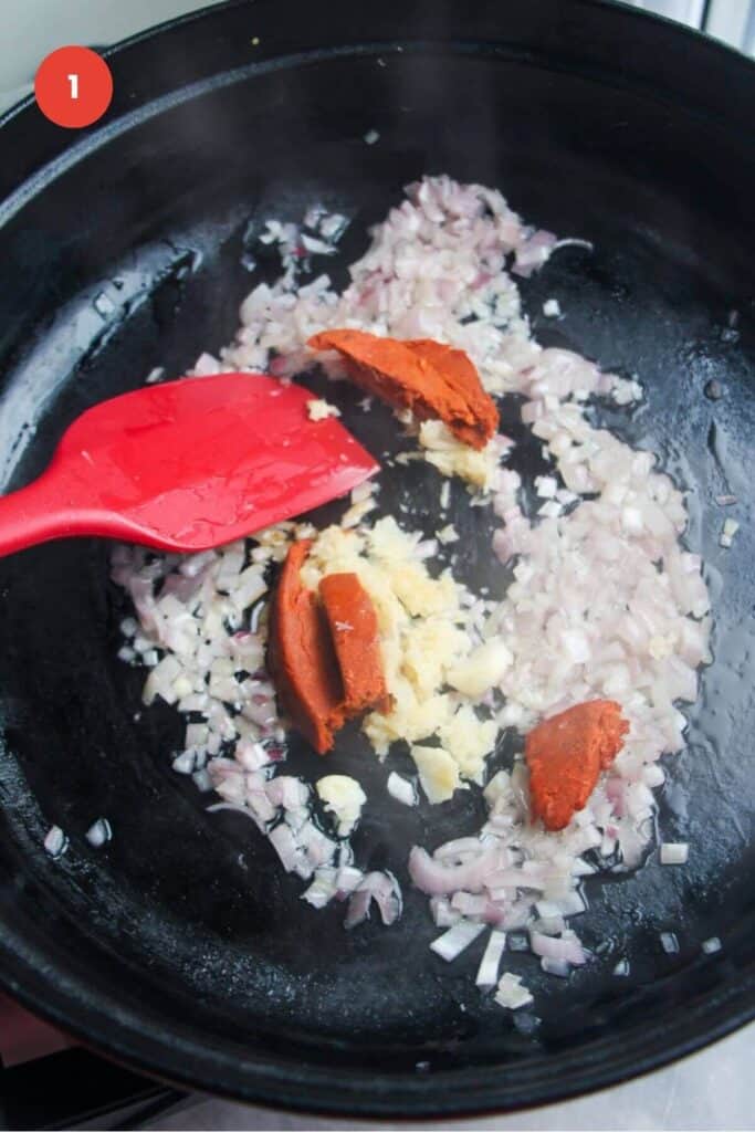 Spatula stirring diced onion and nduja in a large pan.