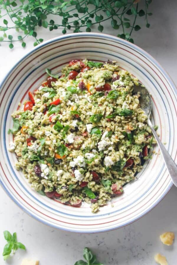 Orzo pesto salad in a large colourful serving bowl with a silver spoon.