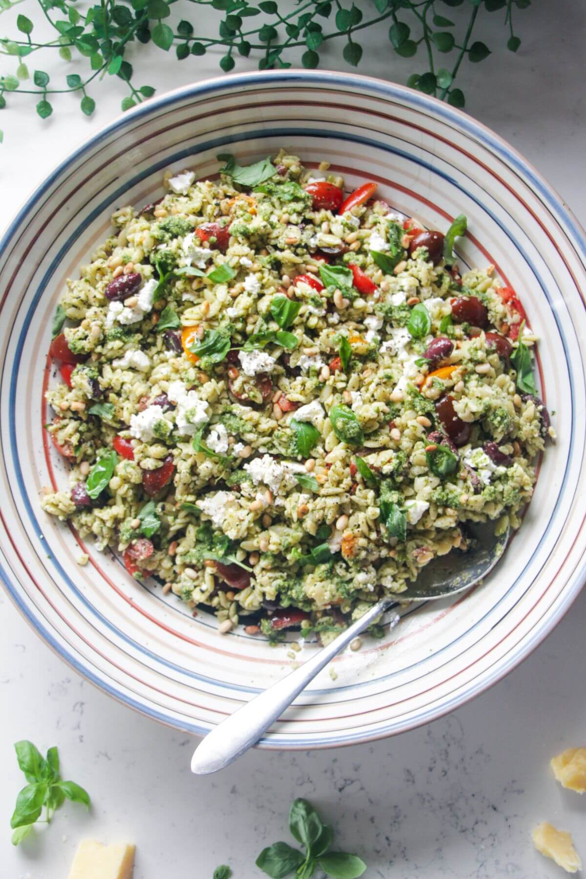 Orzo pesto salad in a large colourful serving bowl with a silver spoon.