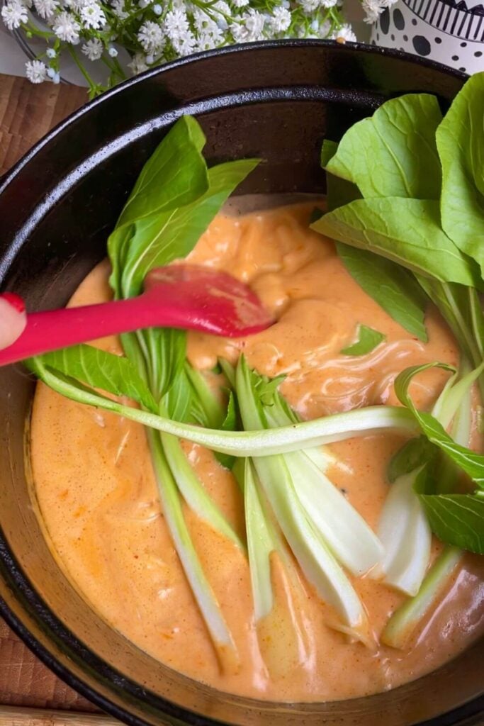 Pak choi added to broth and noodles in pot.