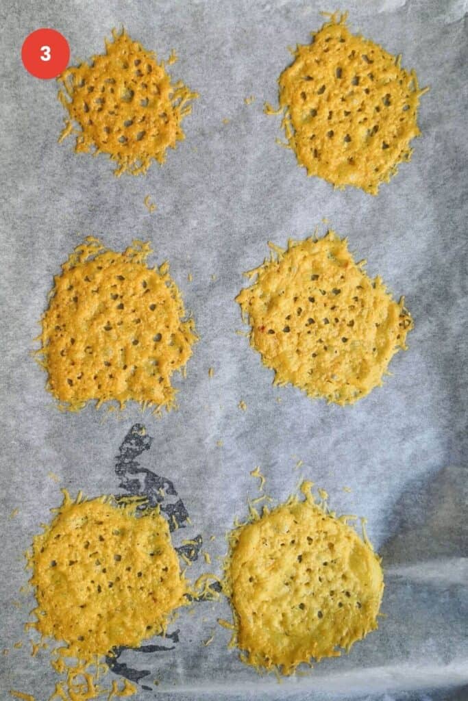 Six parmesan crisps on a baking pan.
