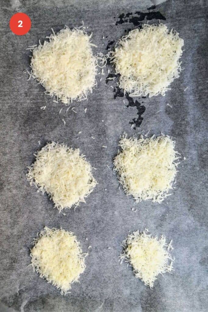 Six piles of grated parmesan cheese on a baking pan.