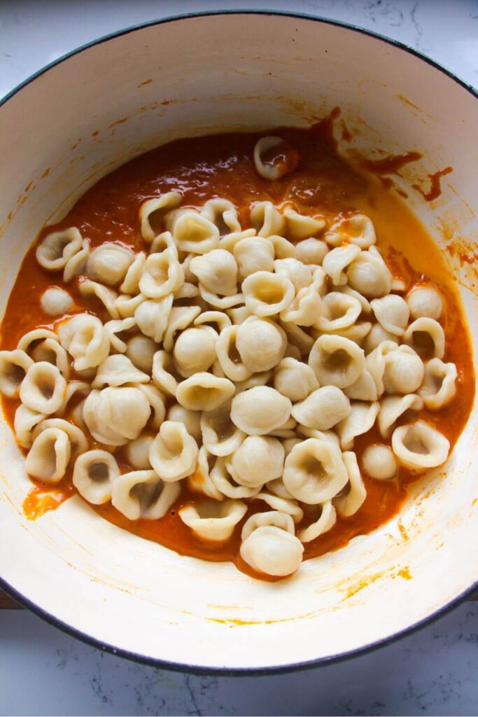 Orecchiette pasta added to a skillet with bright orange gochujang sauce in it.