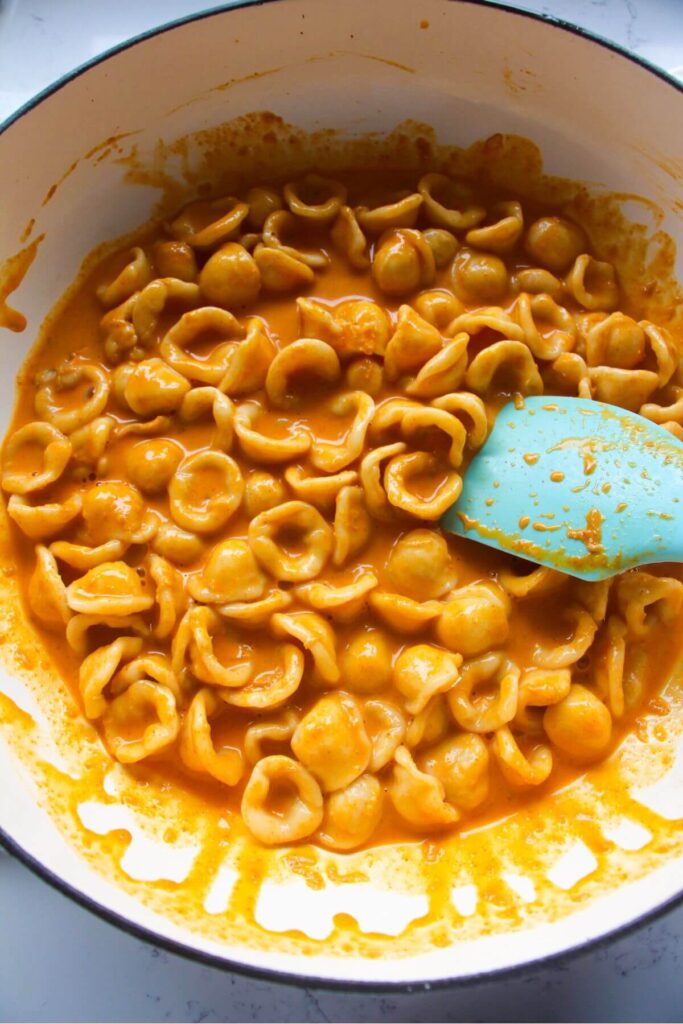 Blue spatula stirring gochujang pasta in a large white skillet.