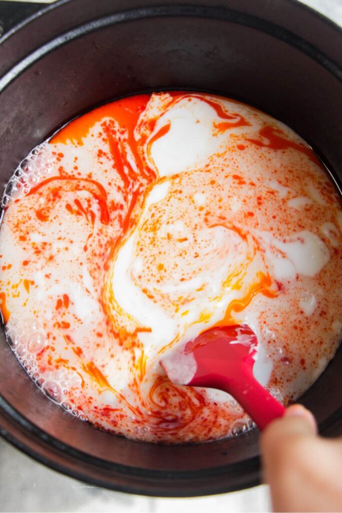 Coconut milk and red paste in a large black pot.