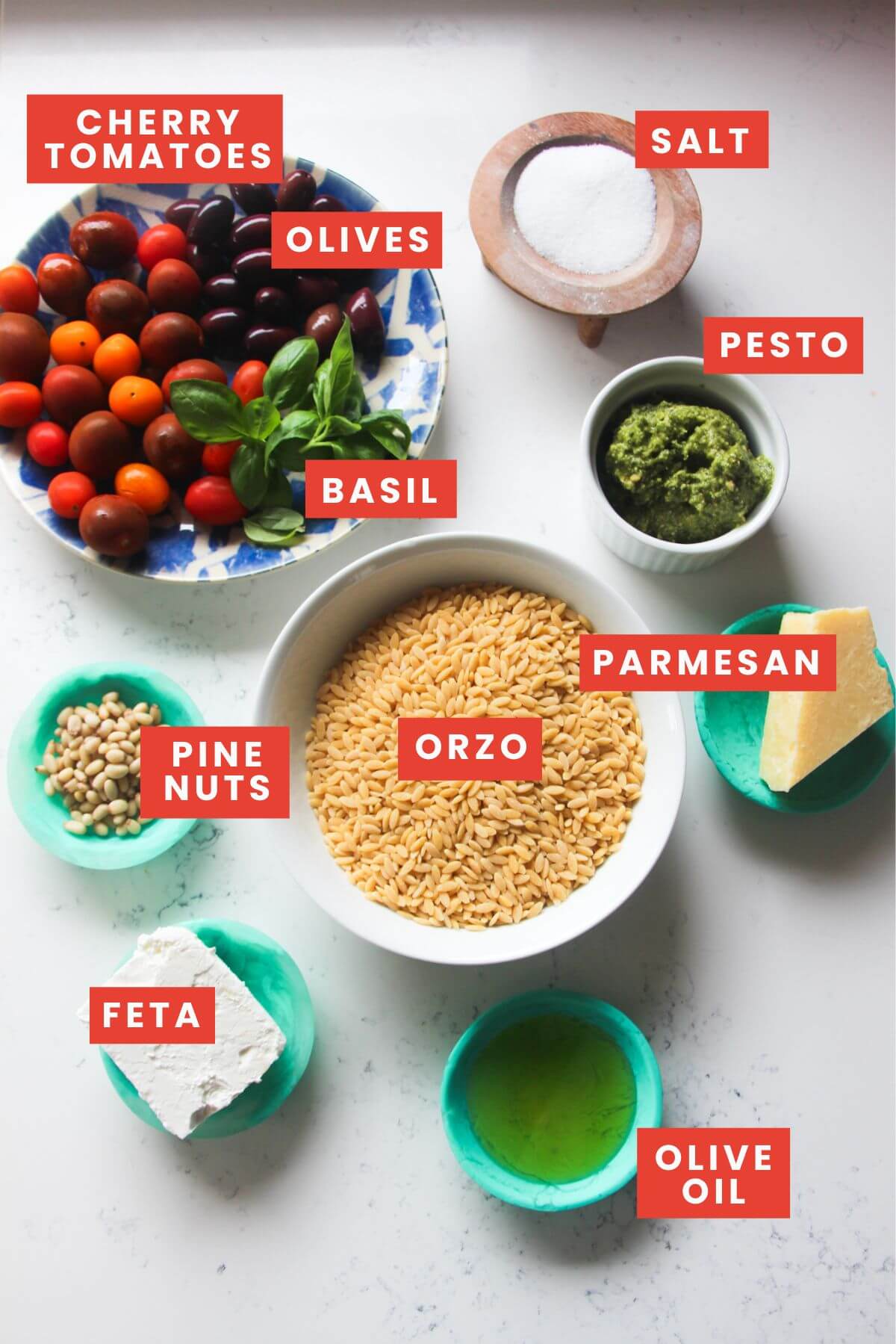 Ingredients for orzo pesto salad laid out on a white marble background and labelled.