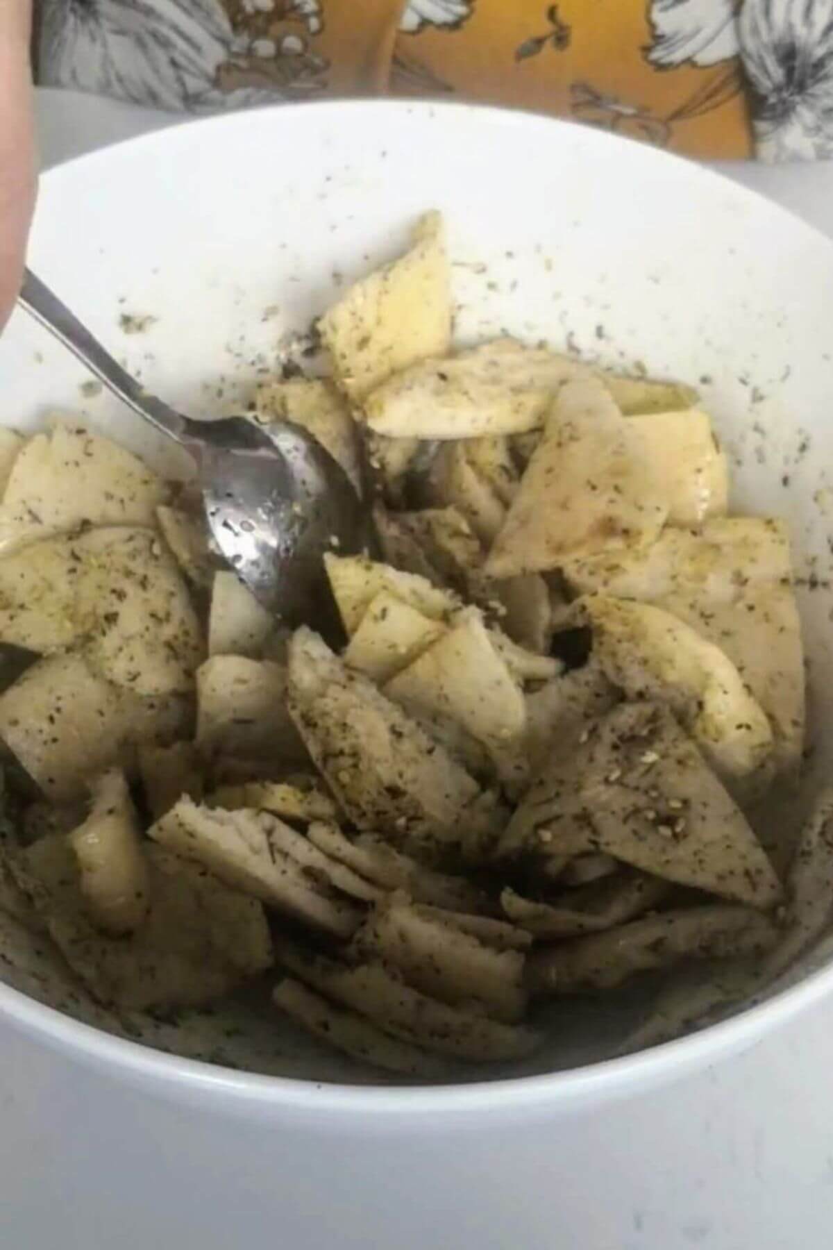 Pita triangles mixed with za'atar oil in a large white bowl.