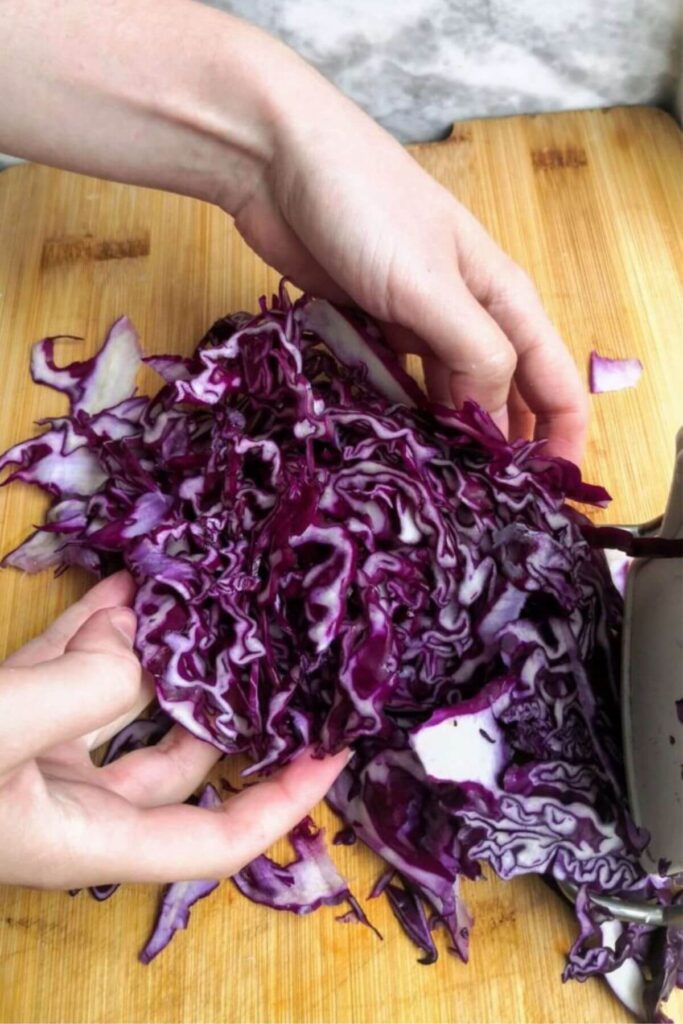 Hands picking up shredded red cabbage on a wooden board.