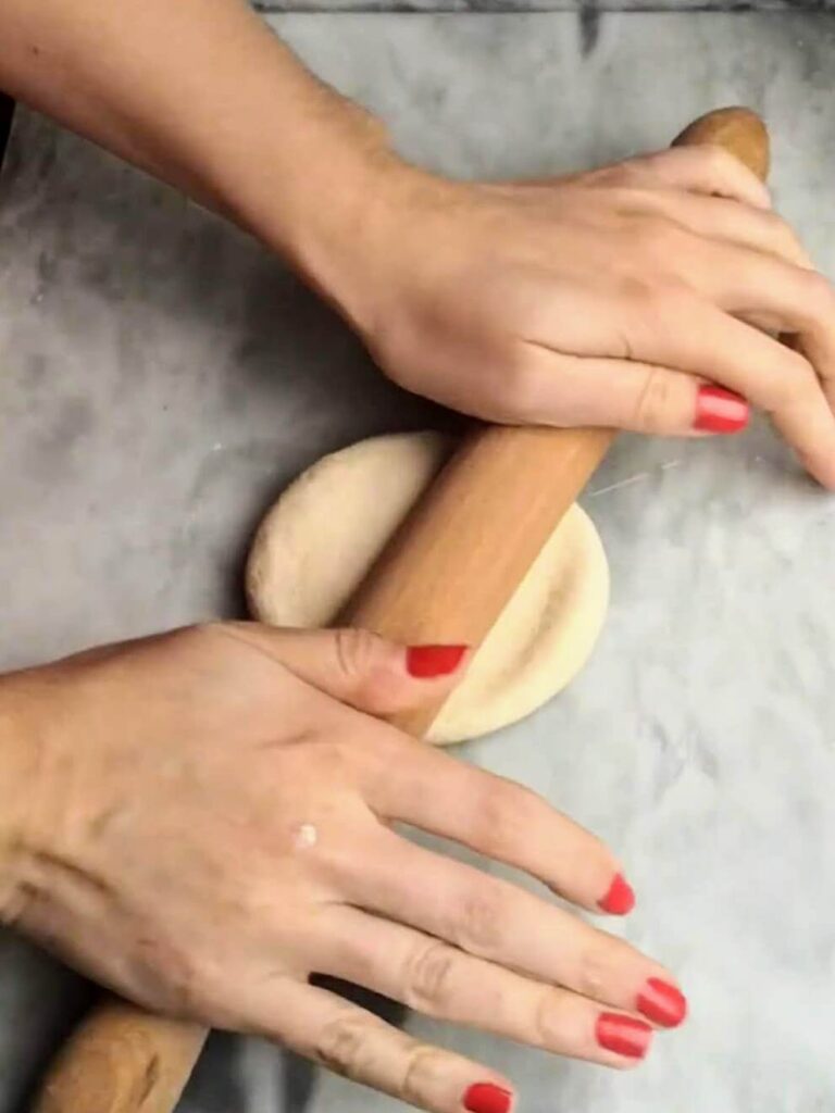 Hands starting to roll out the easy soft flatbread dough with a wooden rolling pin.