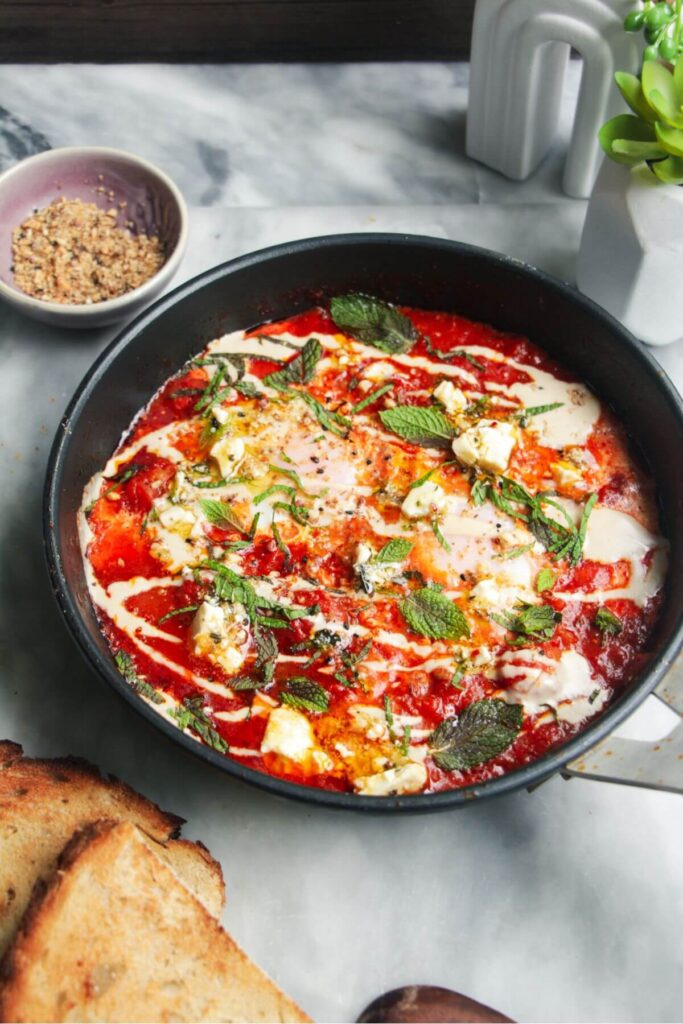 Shakshuka in a small black pan with toast and dukkah on the side.