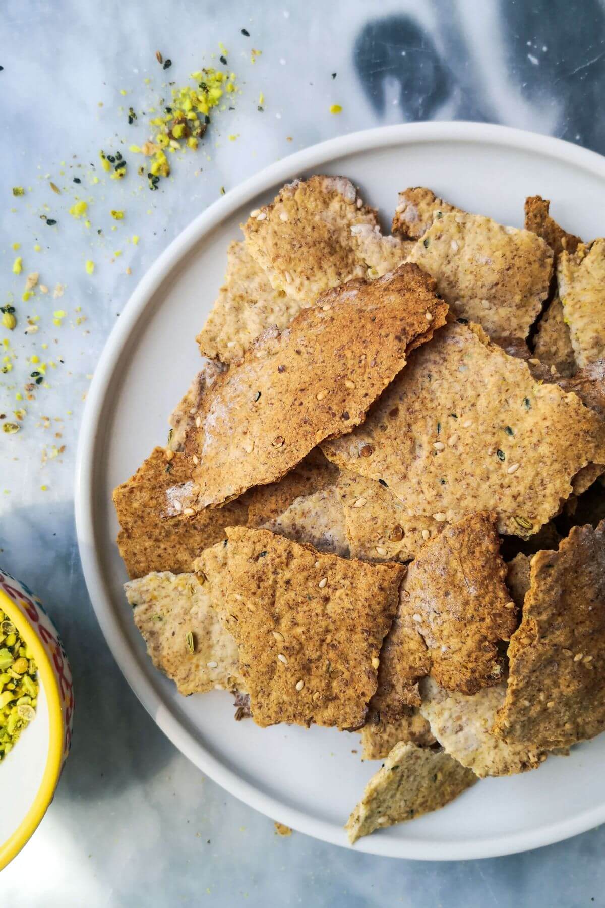 Sourdough crackers on a small white plate with a little bowl of dukkah on the side.