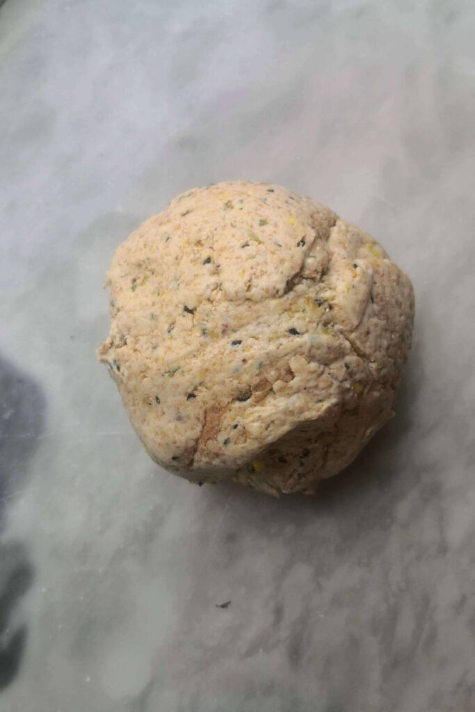 Sourdough discard cracker dough in a ball on a grey marble background.