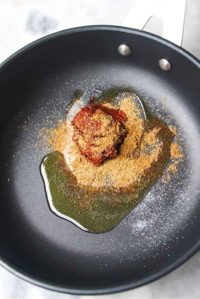 Harissa paste, olive oil and spices in a small black pan.