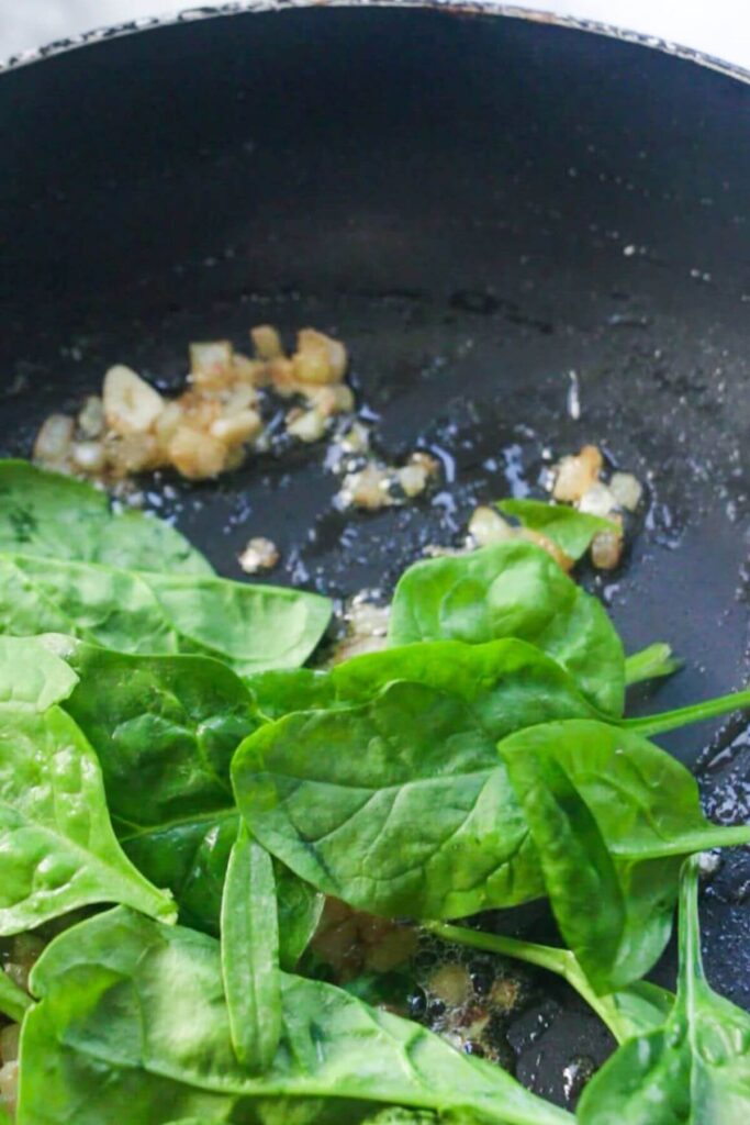 Spinach added to a small pan with shallot.