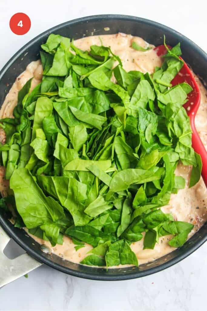 Spinach leaves added to creamy beans in a skillet.