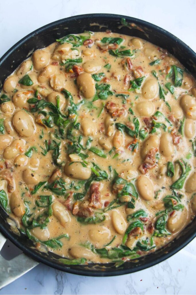 Spinach stirred into creamy white beans in a black frying pan.