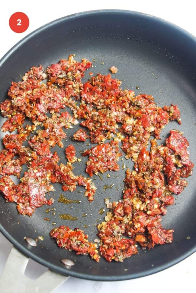 Sundried tomatoes, onion and herbs cooking in a skillet.