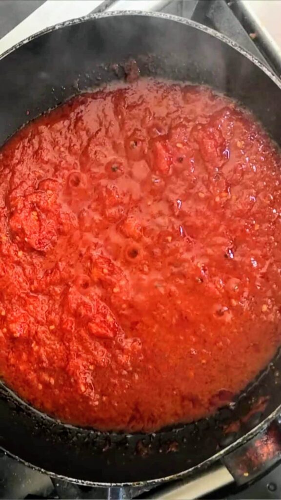 Tomatoes broken down into a thick sauce in a small black pan.