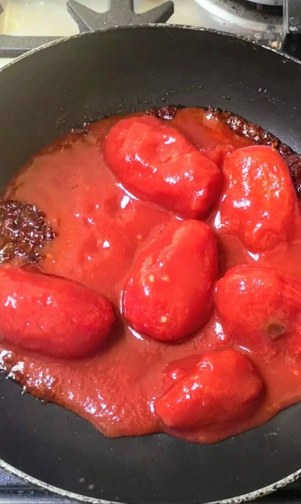 Whole plum tinned tomatoes in a small black pan.