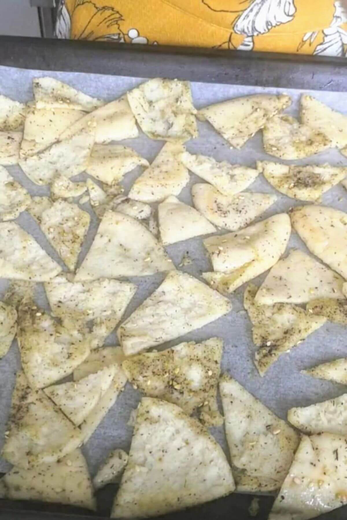 Za'atar brushed pita triangles laid out on a lined oven tray.