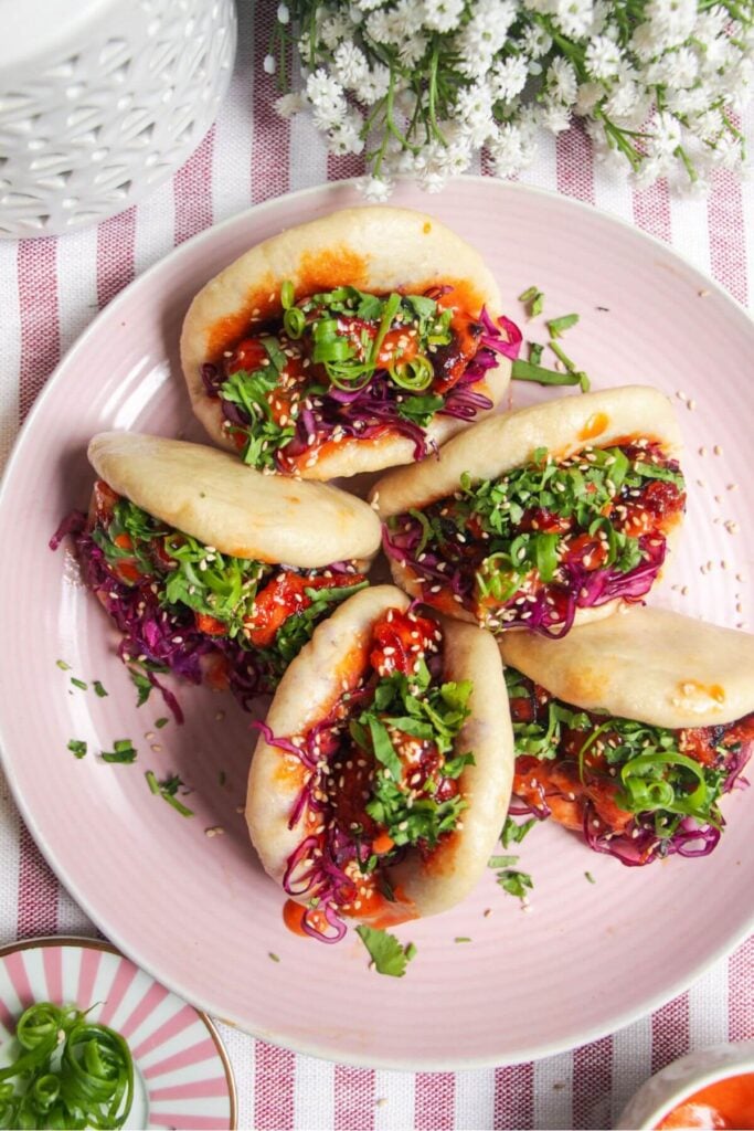 Five Korean chicken filled bao buns on a pink plate with aioli on the side.