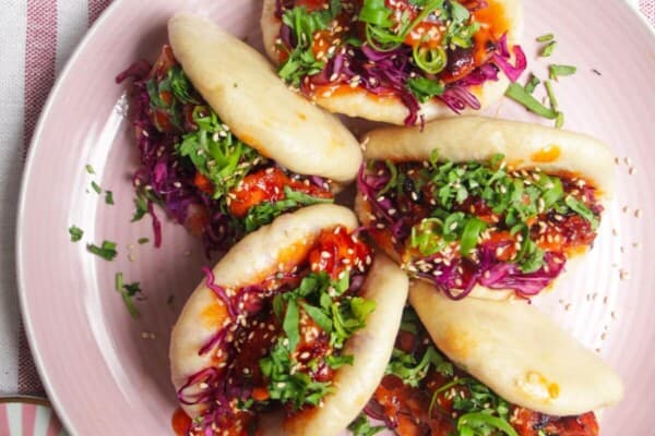 Five Korean chicken filled bao buns on a pink plate with aioli on the side.