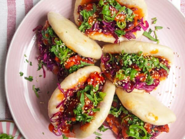 Five Korean chicken filled bao buns on a pink plate with aioli on the side.