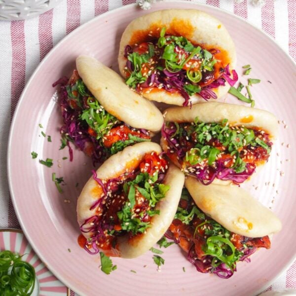 Five Korean chicken filled bao buns on a pink plate with aioli on the side.