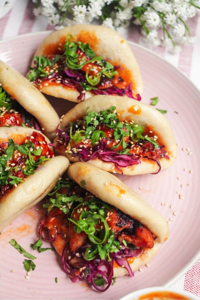 Five Korean chicken filled bao buns on a pink plate with aioli on the side.