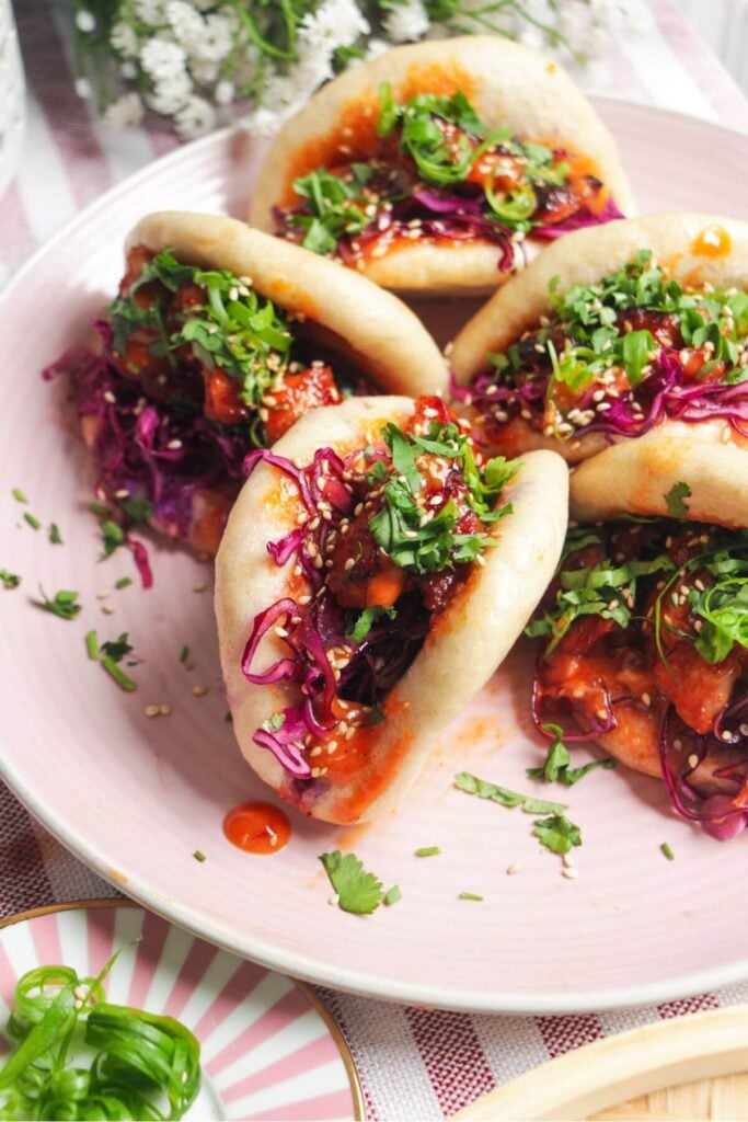 Five Korean chicken filled bao buns on a pink plate with aioli on the side.