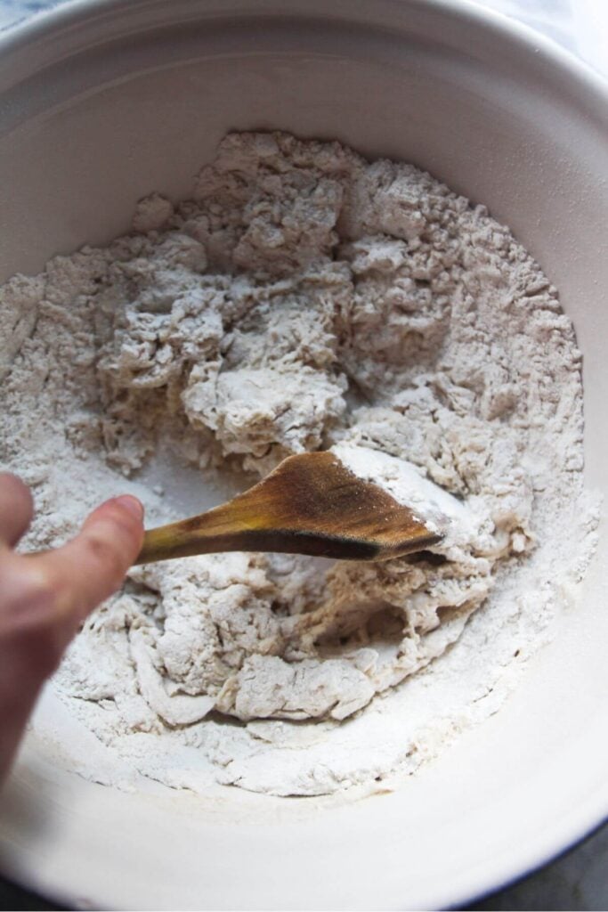 Bao ingredients in a large silver mixing bowl, with water being poured in.