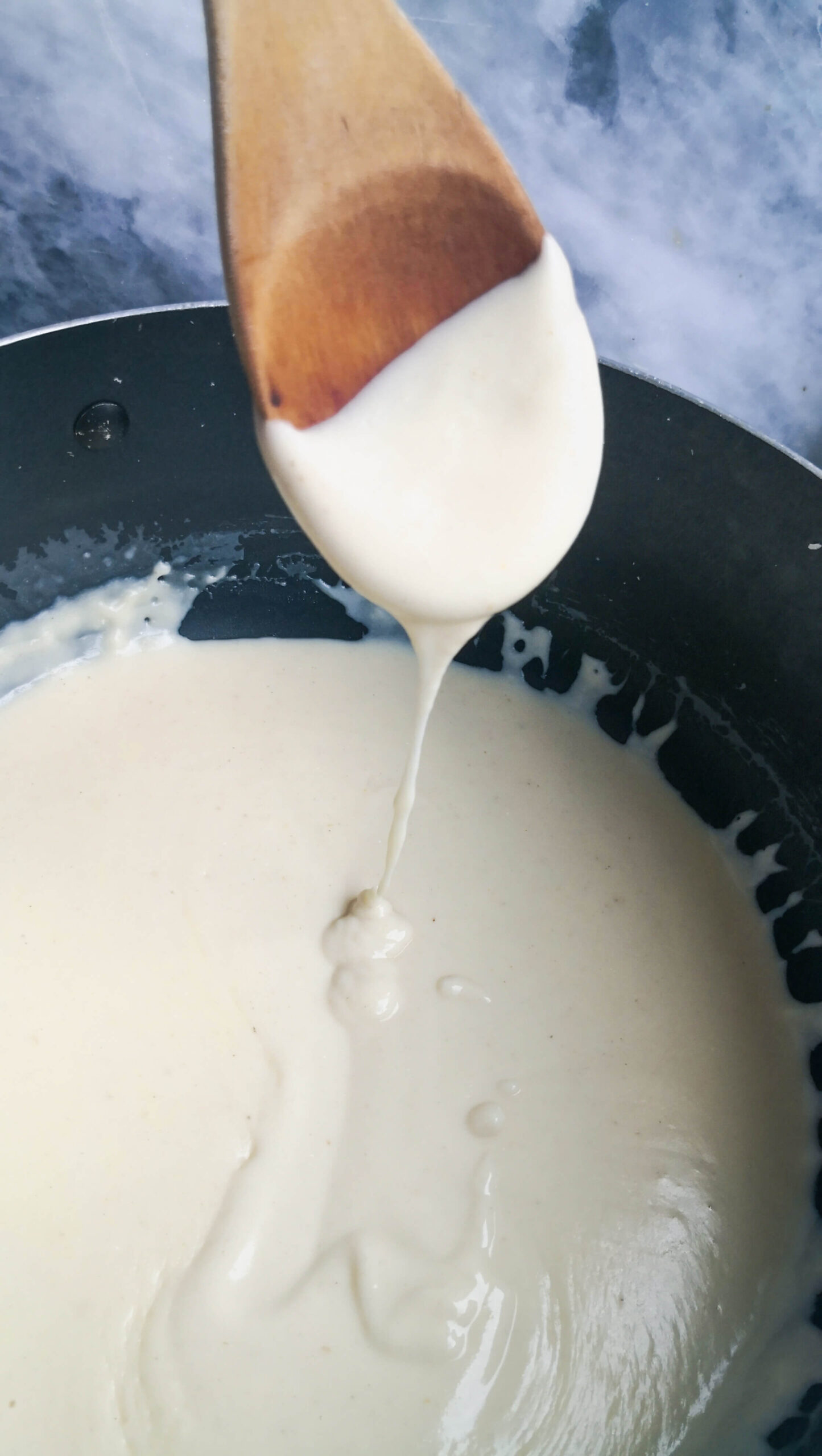 Close up of cheese sauce dripping off spoon into pot of sauce.