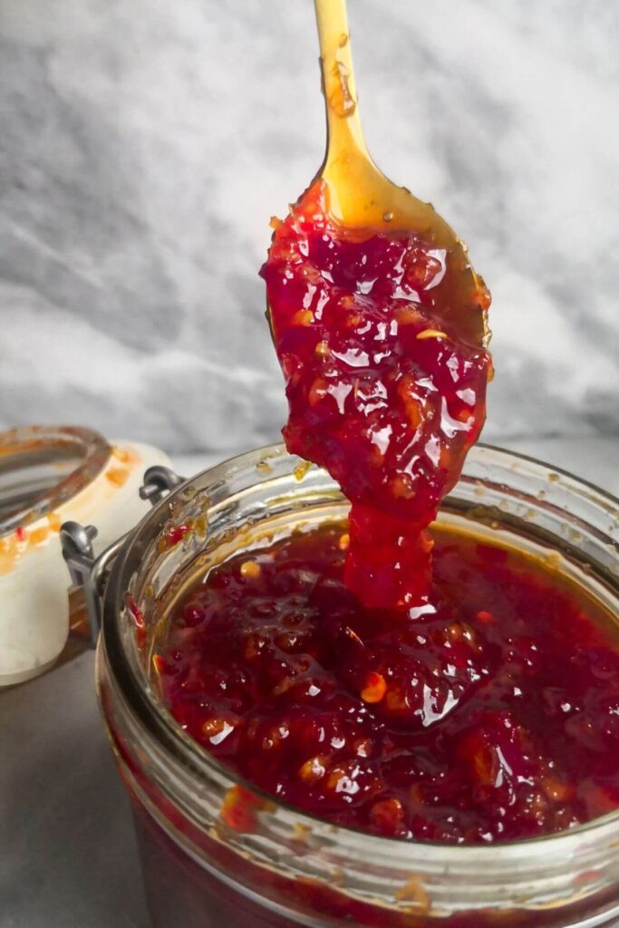 Chilli jam falling off small gold spoon into glass jar.