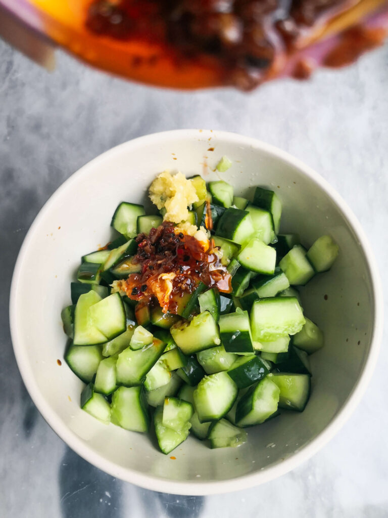 Pouring chilli oil into a small bowl filled with cucumber chunks.