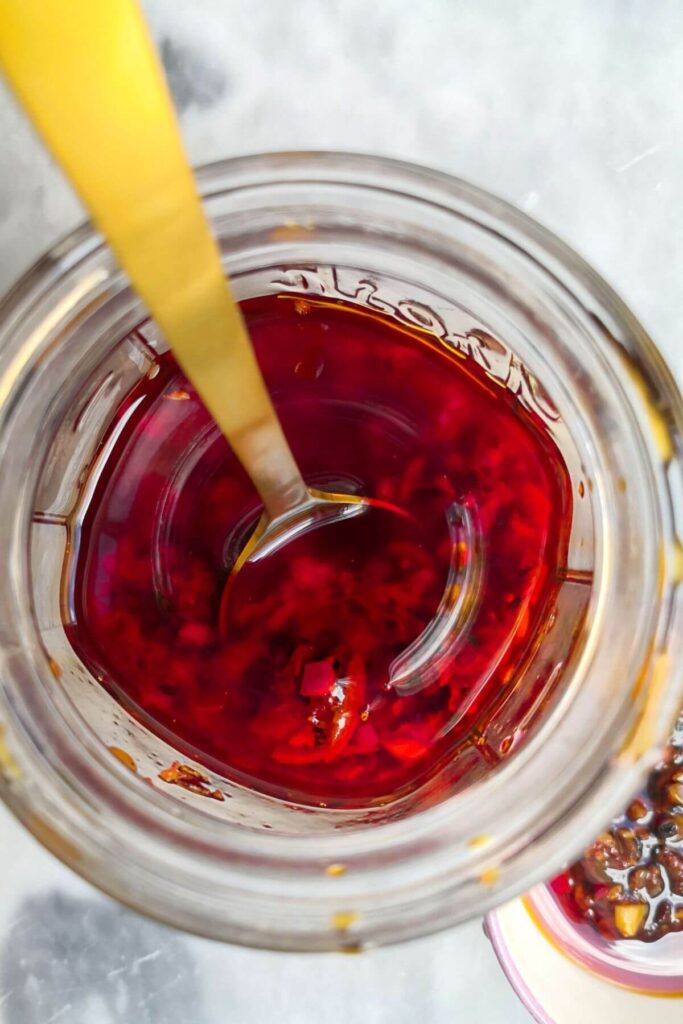 Chilli oil in glass jar with a gold spoon inside, looking from above.